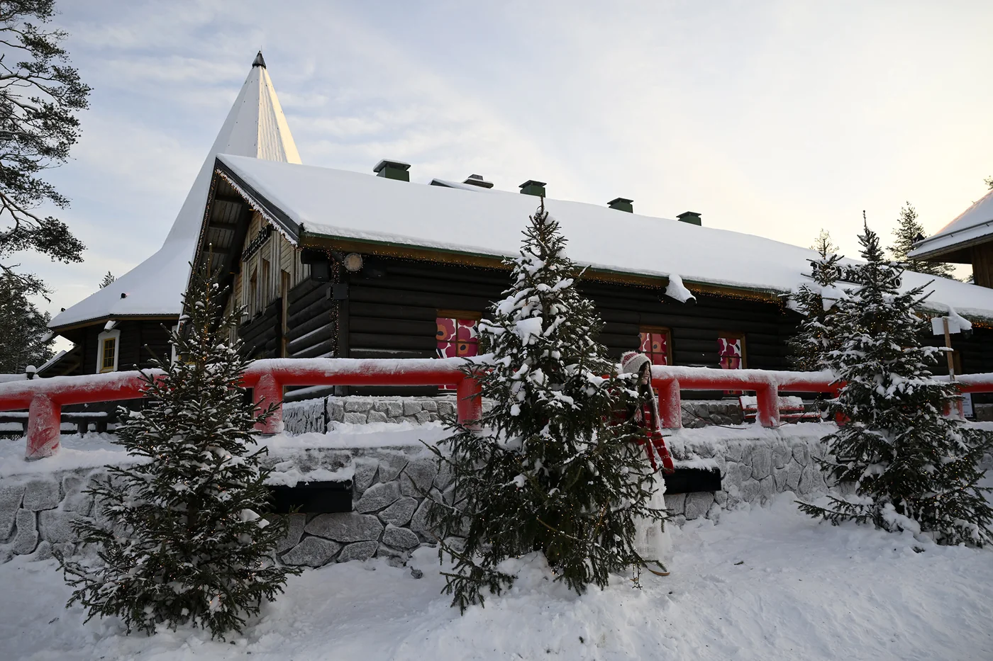 Snedækkede træbygninger og grantræer i Julemandens landsby i Rovaniemi.